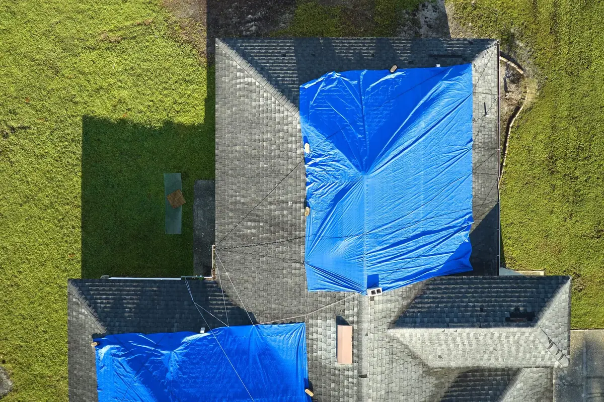 Aerial view of blue emergency tarps covering a storm damaged shingle roof