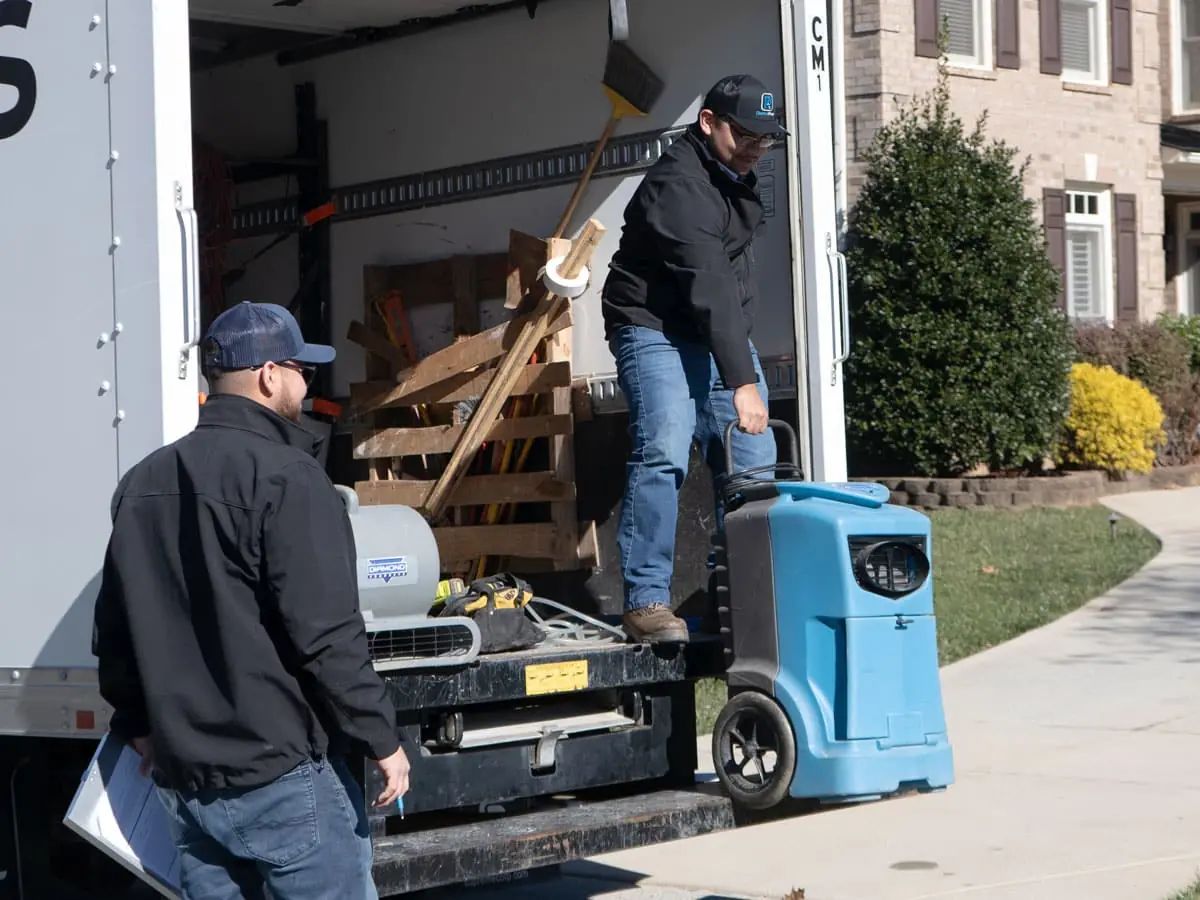 Two Tukwila Water Damage Pros crew members unloading drying equipment from an unmarked service truck