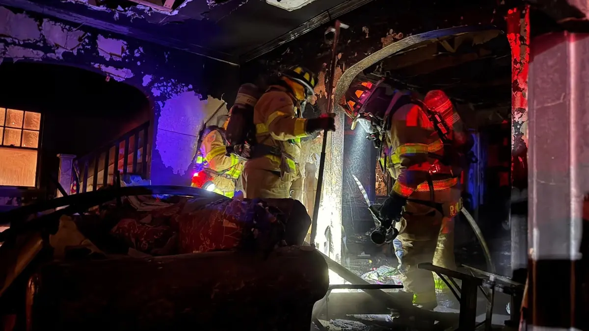 Firefighter spraying water inside a fire-damaged home interior